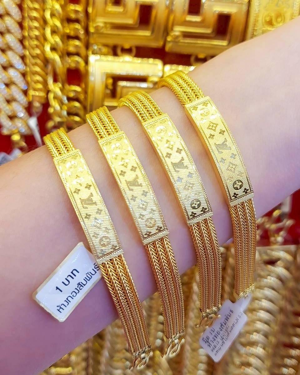 Close-up of four 23K Thai gold link bracelets on a wrist, featuring a distinctive Louis Vuitton-style geometric pattern and indicated as 1 Baht weight.