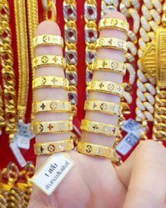 Close-up of stackable 23K Thai gold rings featuring a polished surface and a geometric Louis Vuitton-style monogram pattern.