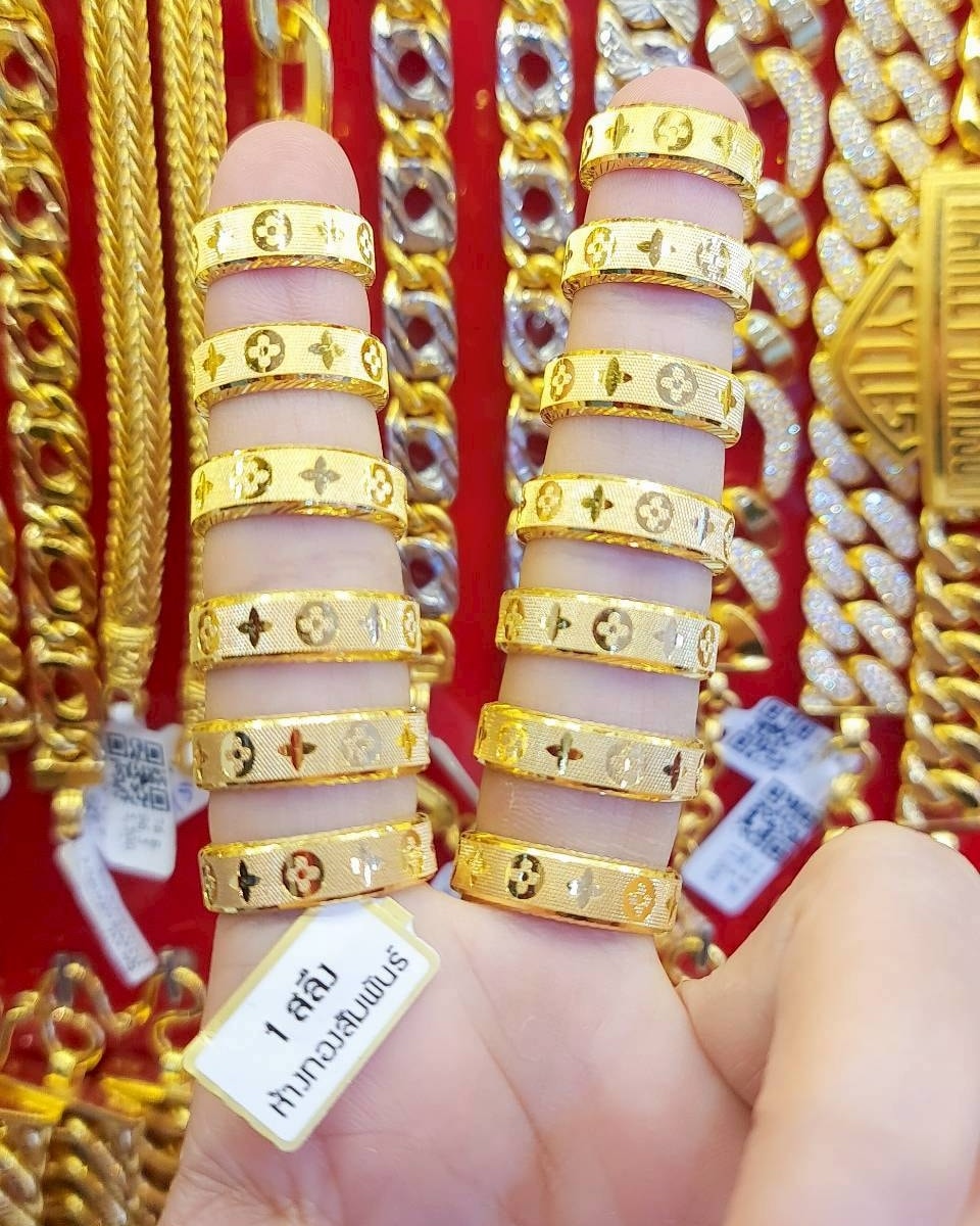 Close-up of stackable 23K Thai gold rings featuring a polished surface and a geometric Louis Vuitton-style monogram pattern.